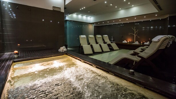 Une salle de spa équipée d’un bain à remous, de plusieurs chaises longues et de bougies.