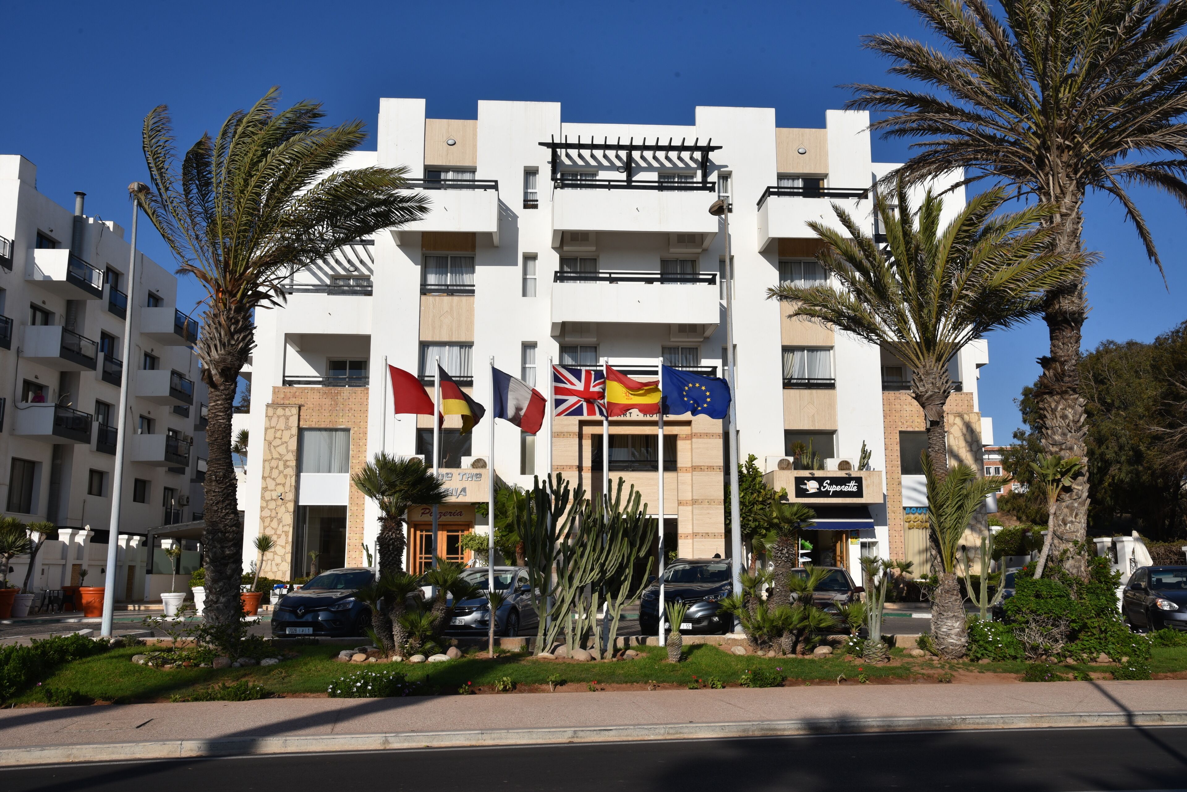 A multi-story building with balconies, palm trees, and flags.