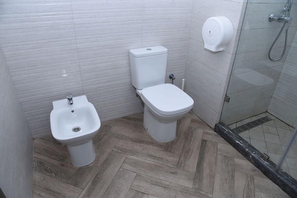 A bathroom with a bidet, toilet, and a hand dryer.