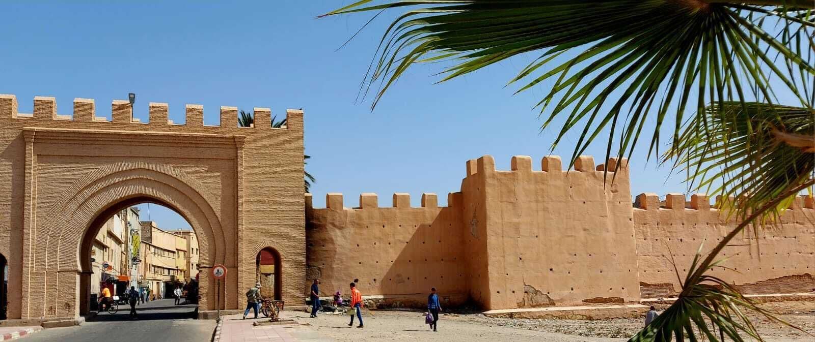 Un grand arc en pierre mène à un mur fortifié, avec un ciel dégagé au-dessus.