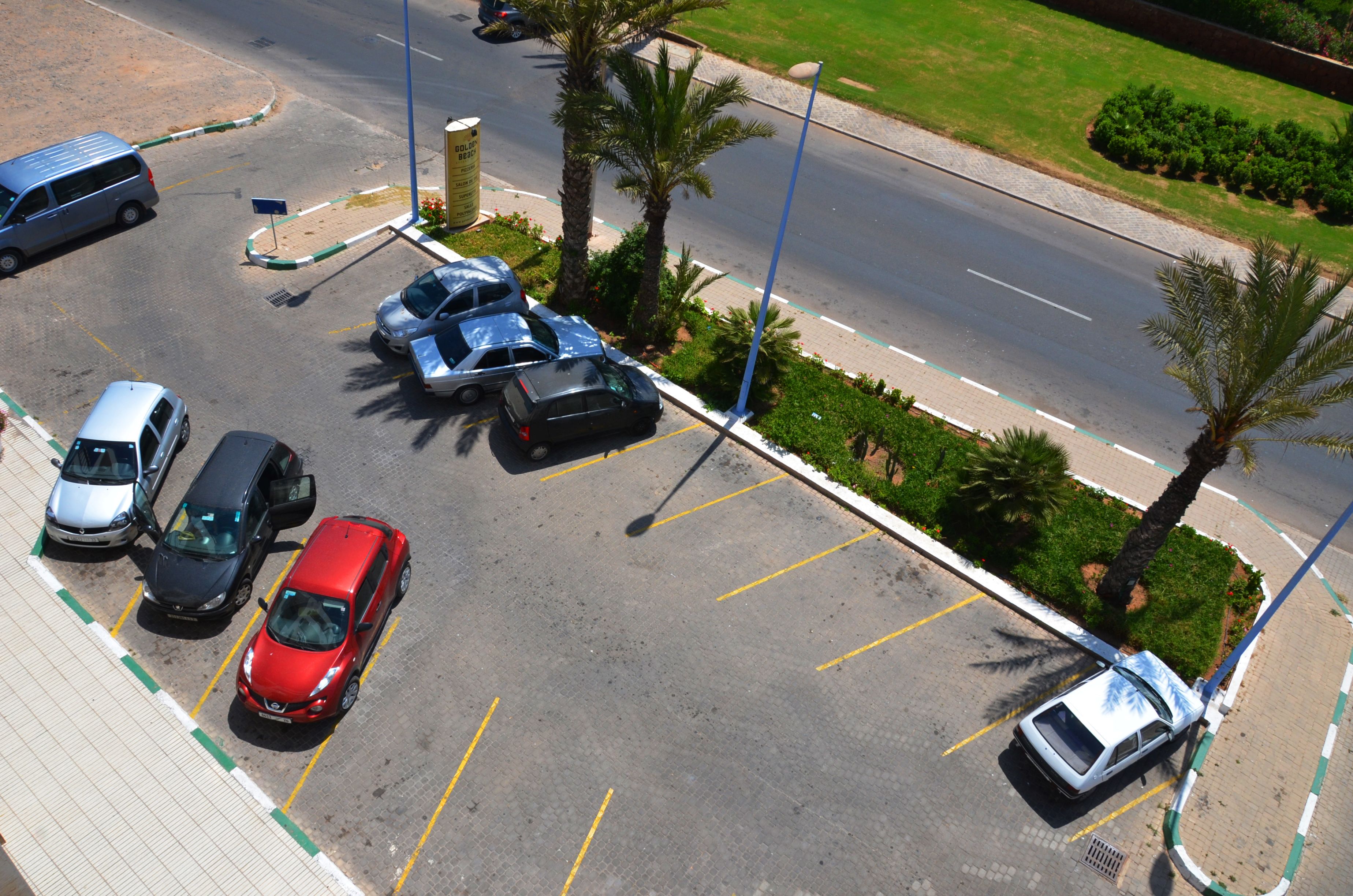 Un estacionamiento con varios coches, un autobús y palmeras.