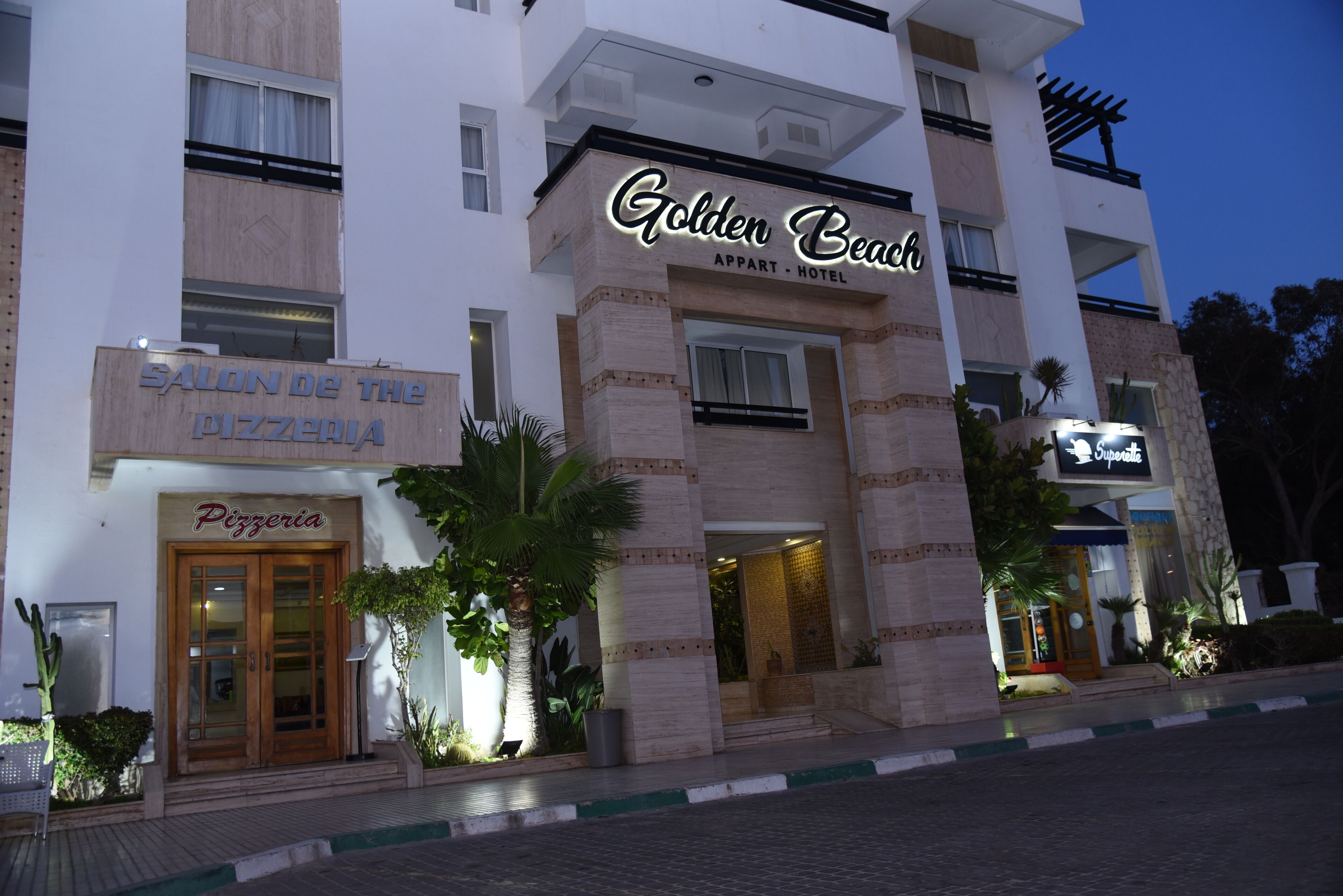 Ein Hotel mit einem Schild, das „Golden Beach“ zeigt, und einer Pizzeria namens „Salon de la Pizzeria“ im Erdgeschoss.