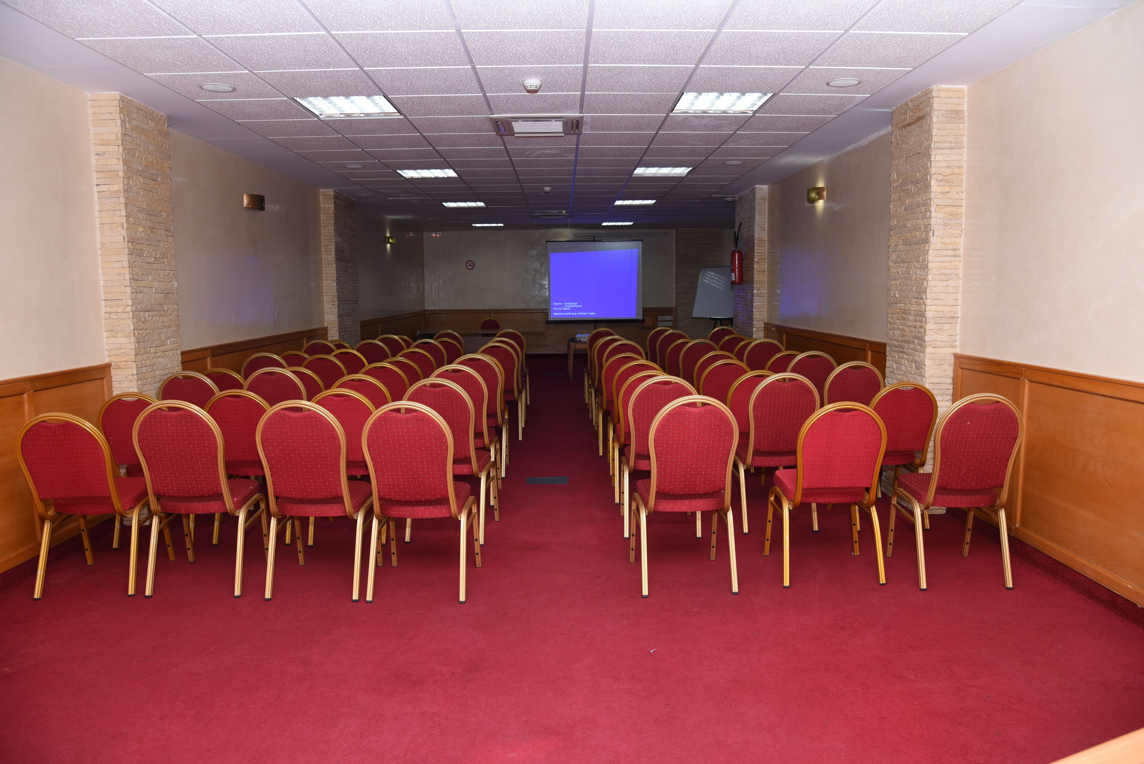 A conference room with rows of red chairs, a projector screen, and a carpeted floor.