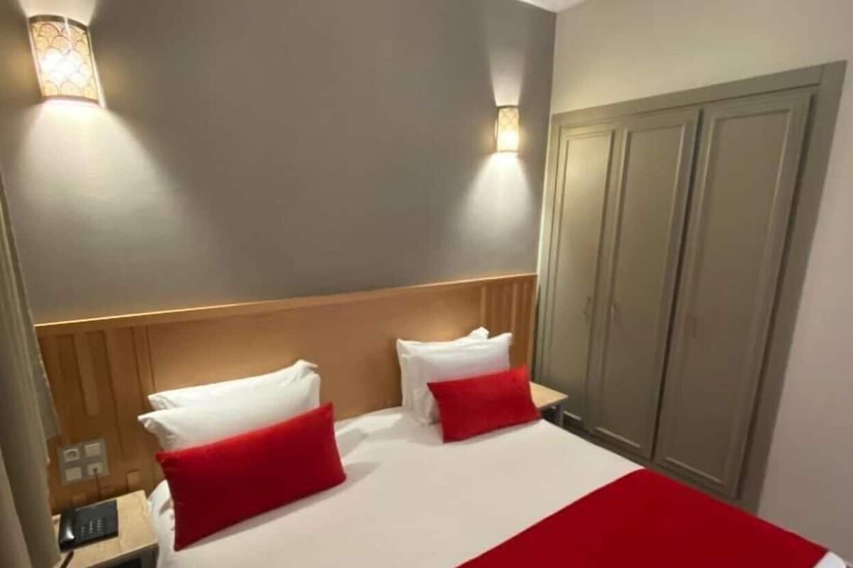 Ett hotellrum med en sÀng, sÀngbord, en garderob och vÀggmonterad belysning.