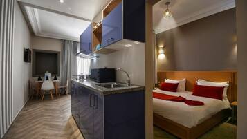 Una habitación de hotel compacta con kitchenette, una cama con almohadas rojas y una pequeña zona de comedor.
