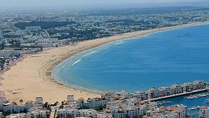 A coastal cityscape with a wide beach, a marina with boats, and residential buildings. - Golden Beach Appart'hotel (Agadir)