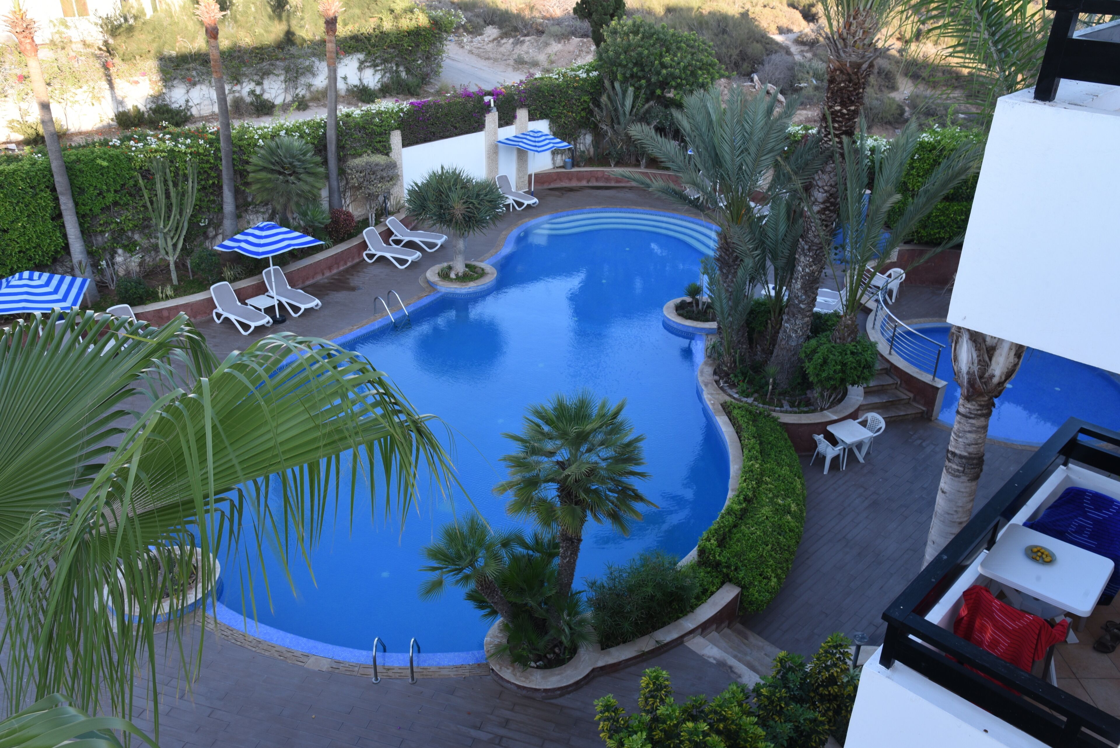 Ein Swimmingpool, umgeben von Liegestühlen und Sonnenschirmen, mit Palmen und Blick auf die umliegende Landschaft.