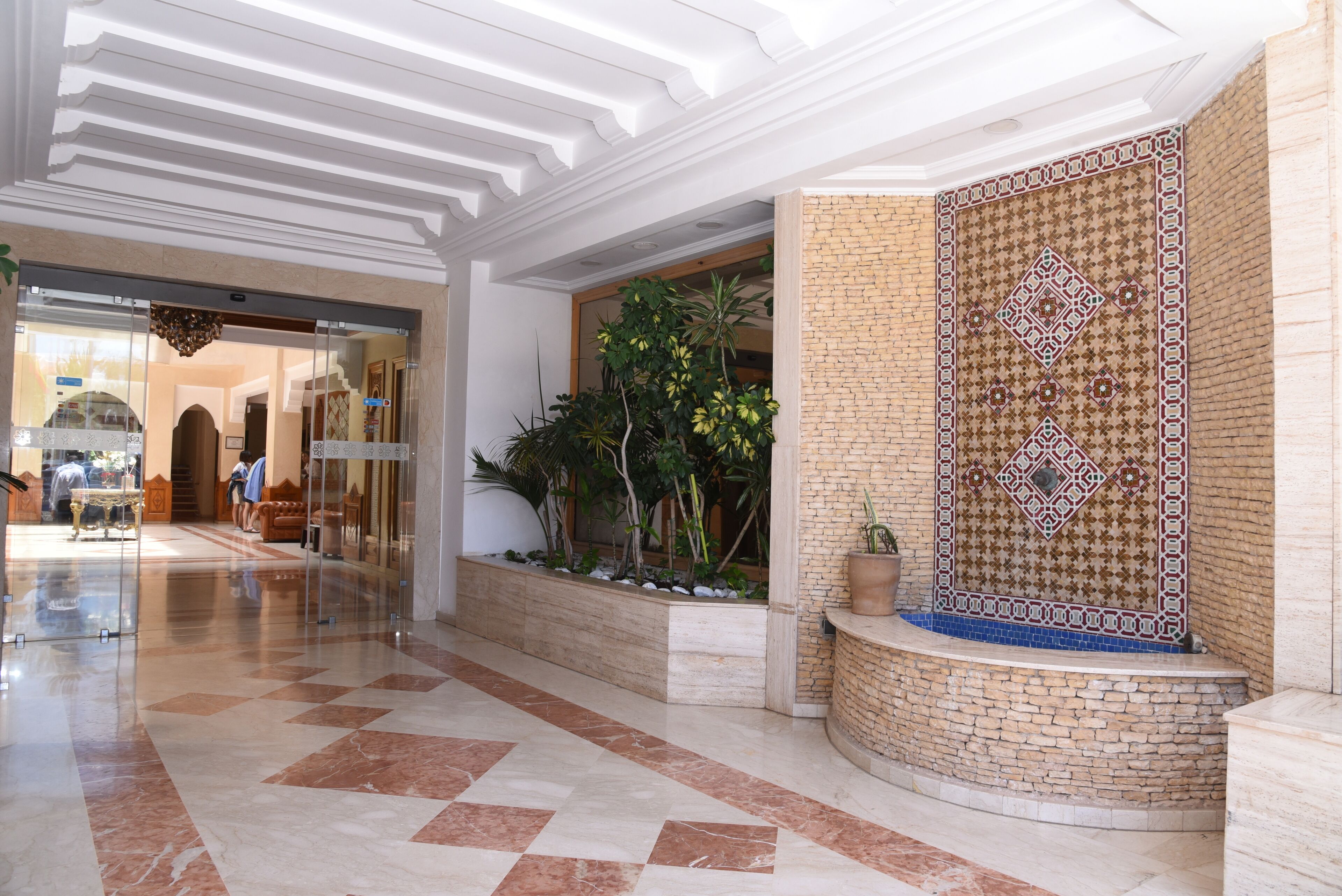 Un vestíbulo con piso a cuadros, pared de ladrillo con diseño de baldosas y una jardinera con plantas.
