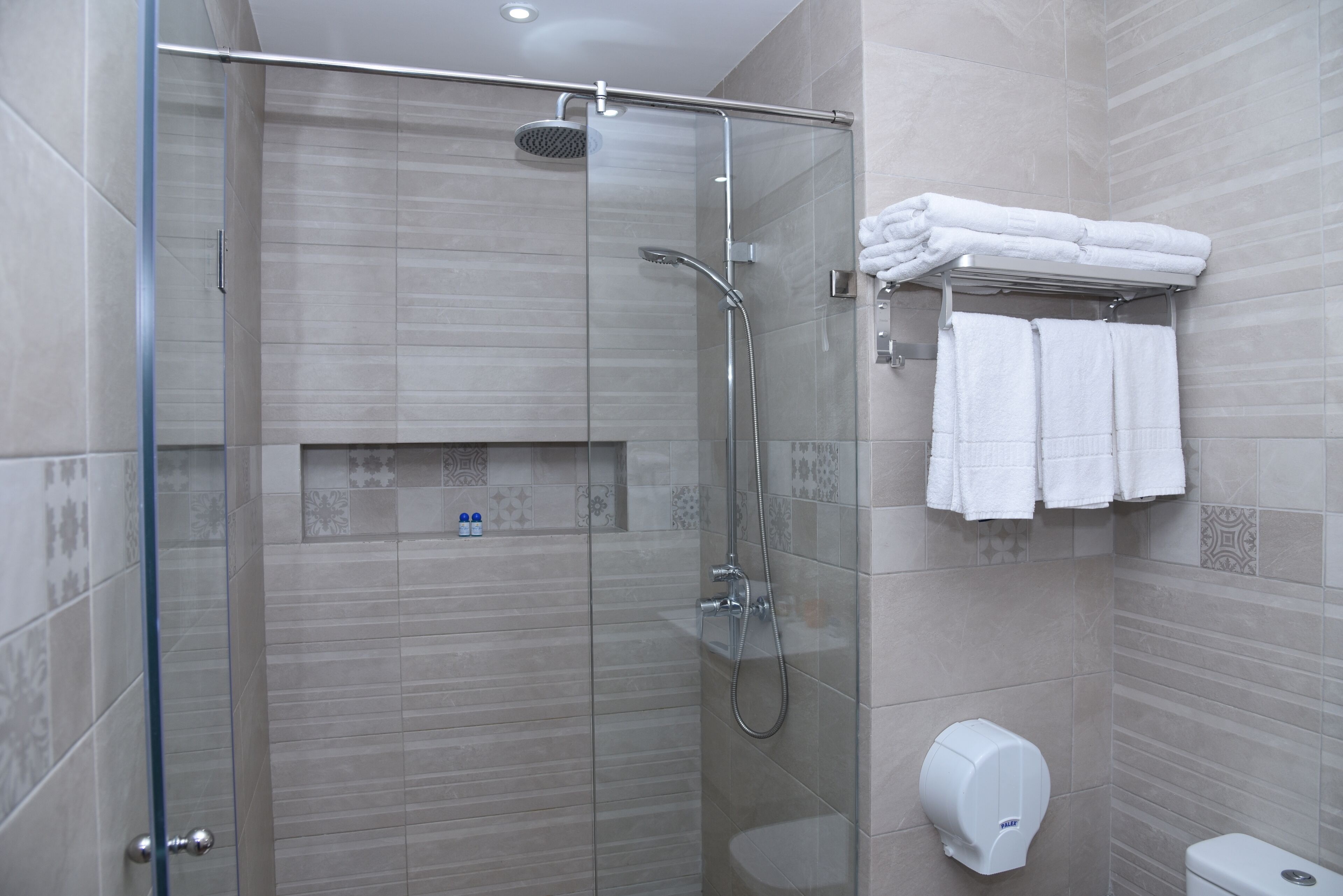 Ein modernes Badezimmer mit einer gläsernen Duschkabine, einer Toilette und einem Handtuchhalter mit gefalteten Handtüchern.