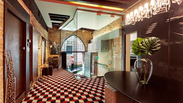 Un hall d’hôtel avec un sol à carreaux, une grande plante et un lustre moderne.