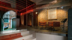Un hall d’entrée moderne avec un mur de verre, un escalier aux marches rouges et un espace détente avec deux fauteuils orange.