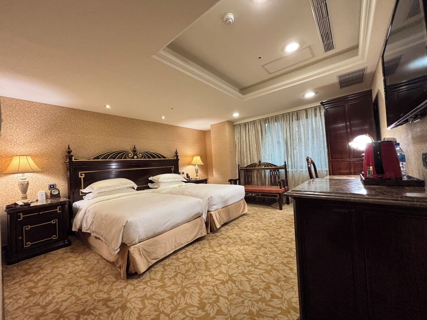 Habitación de hotel con dos camas, un escritorio, una silla, televisión y un minibar.