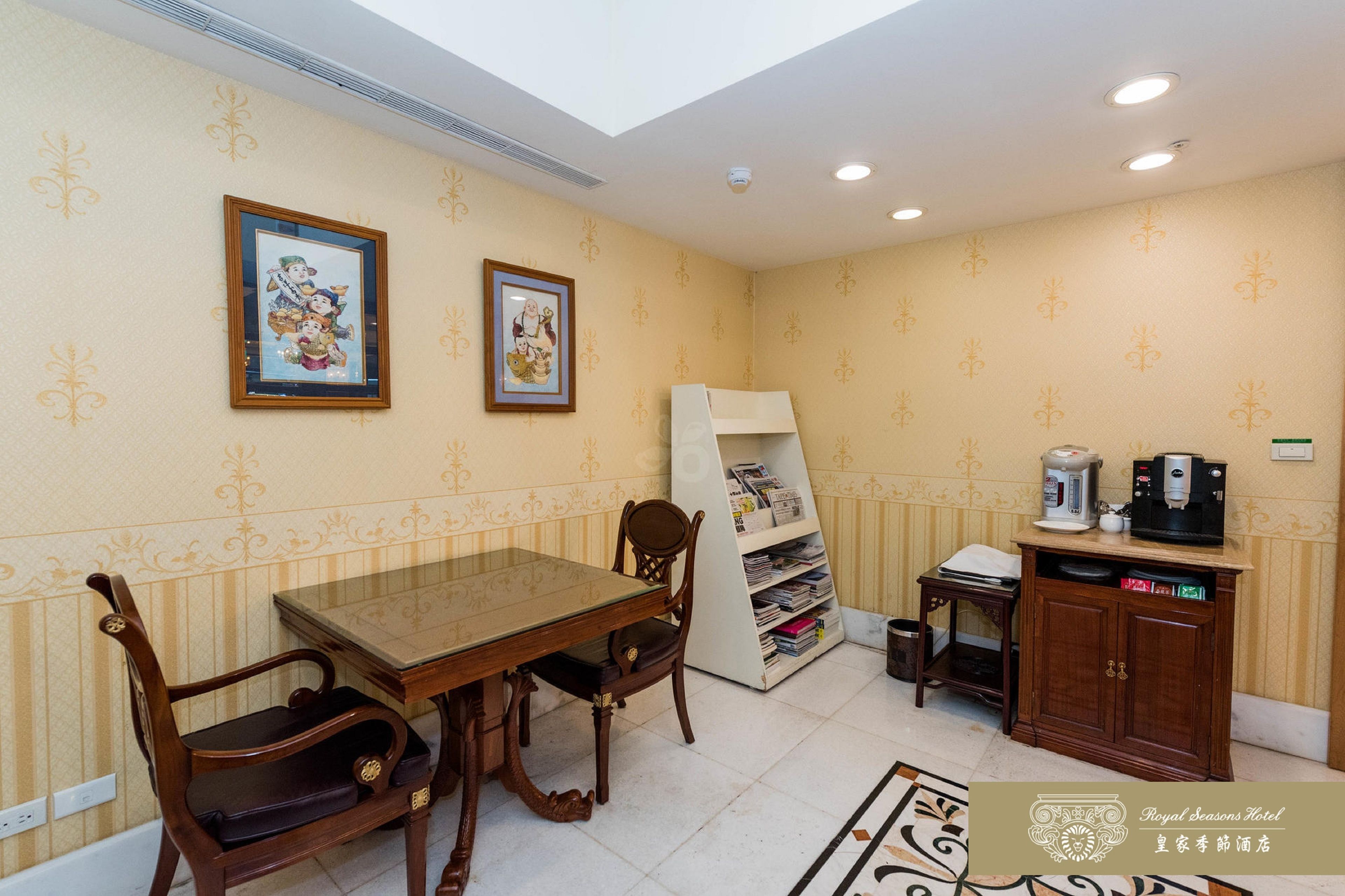 A hotel room with a dining table, chairs, a bookshelf, a cabinet with a coffee machine, and two framed pictures on the wall.