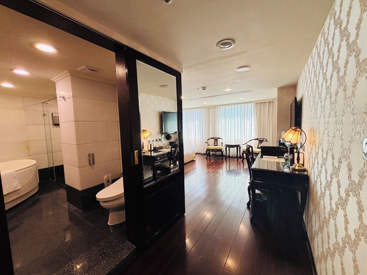 A hotel room with a bathroom, a dining area, and a large mirror.