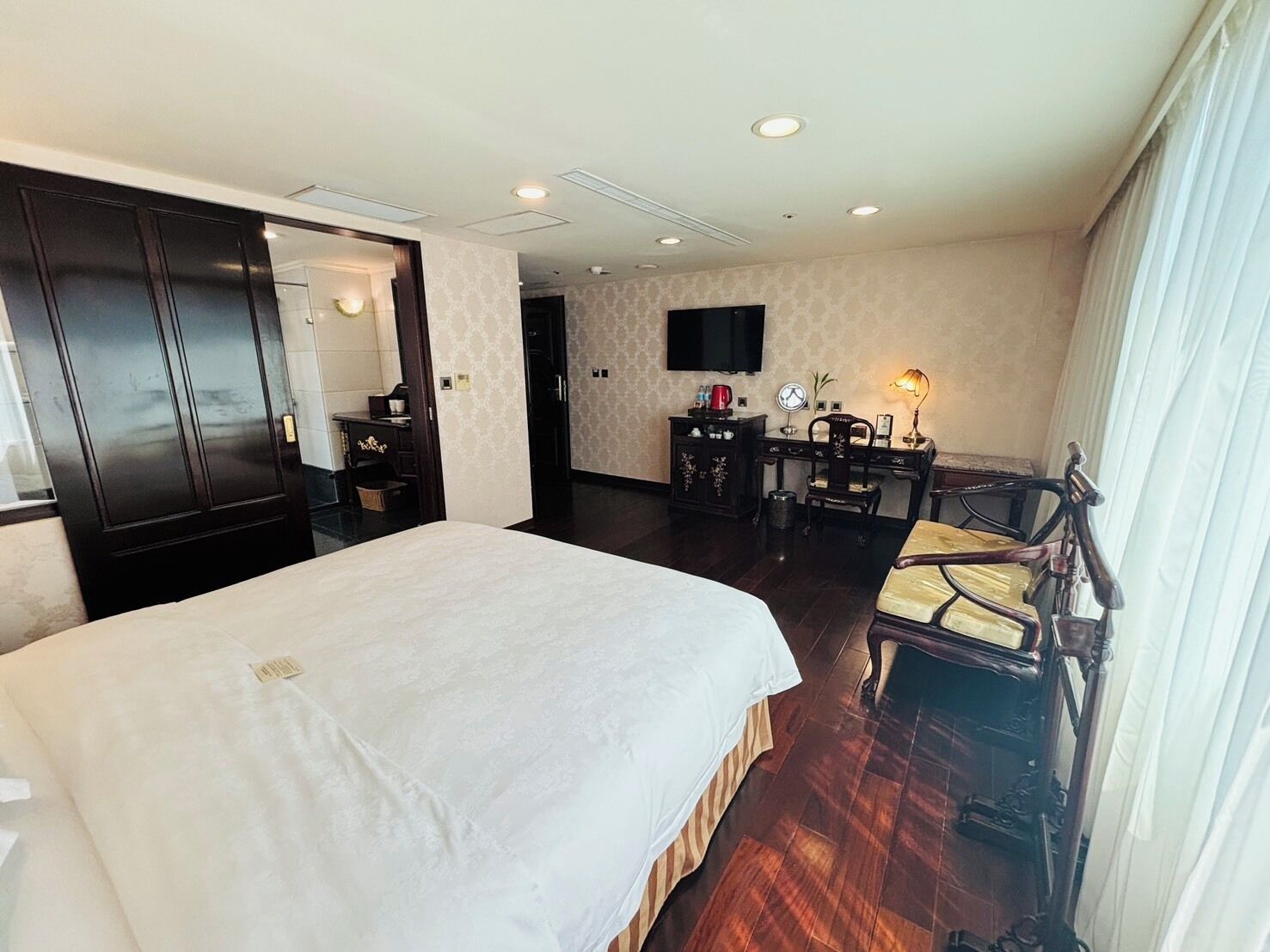 A hotel room with a large bed, a desk with a chair, a television, and a window with curtains.
