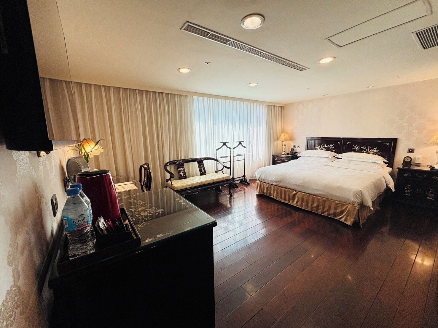 A hotel room with a large bed, a desk with a chair, a wardrobe, and a mirror.