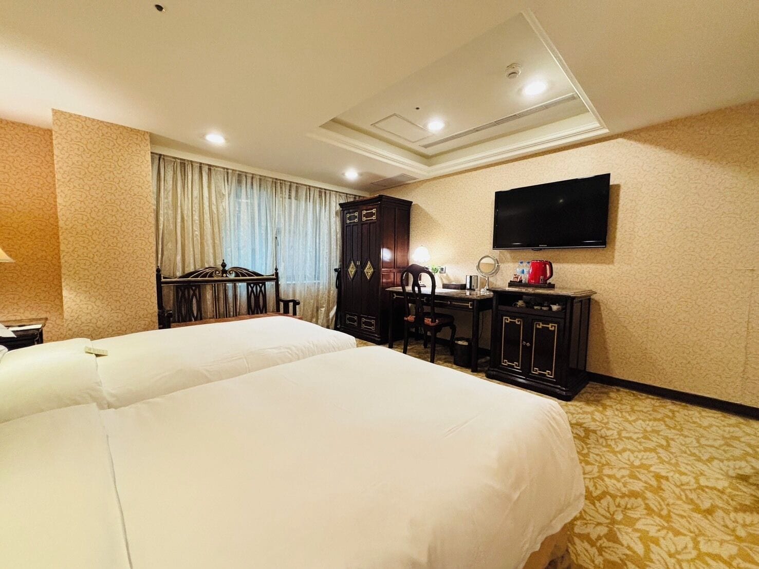 A hotel room with a large bed, a desk, a chair, a wardrobe, a television, and a coffee maker.