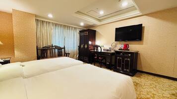 A hotel room with a large bed, a desk, a chair, a wardrobe, a television, and a coffee maker.