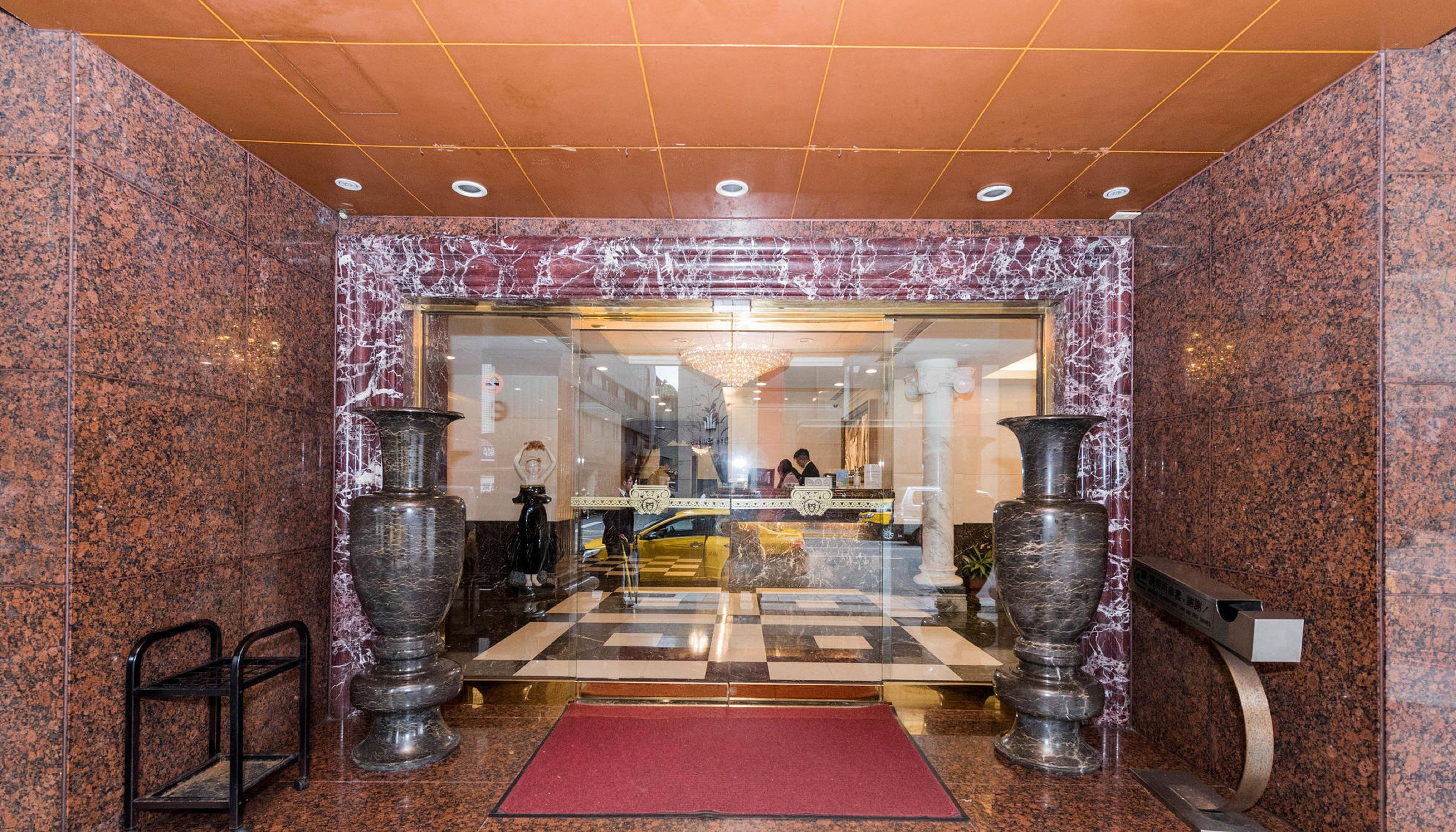 A lobby with a checkered floor, marble walls, and large vases.