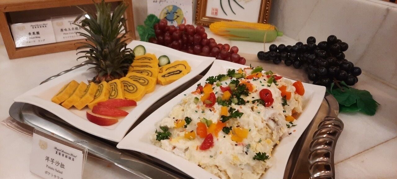 A buffet table with various dishes including a pineapple, sliced fruits, and a salad with vegetables.