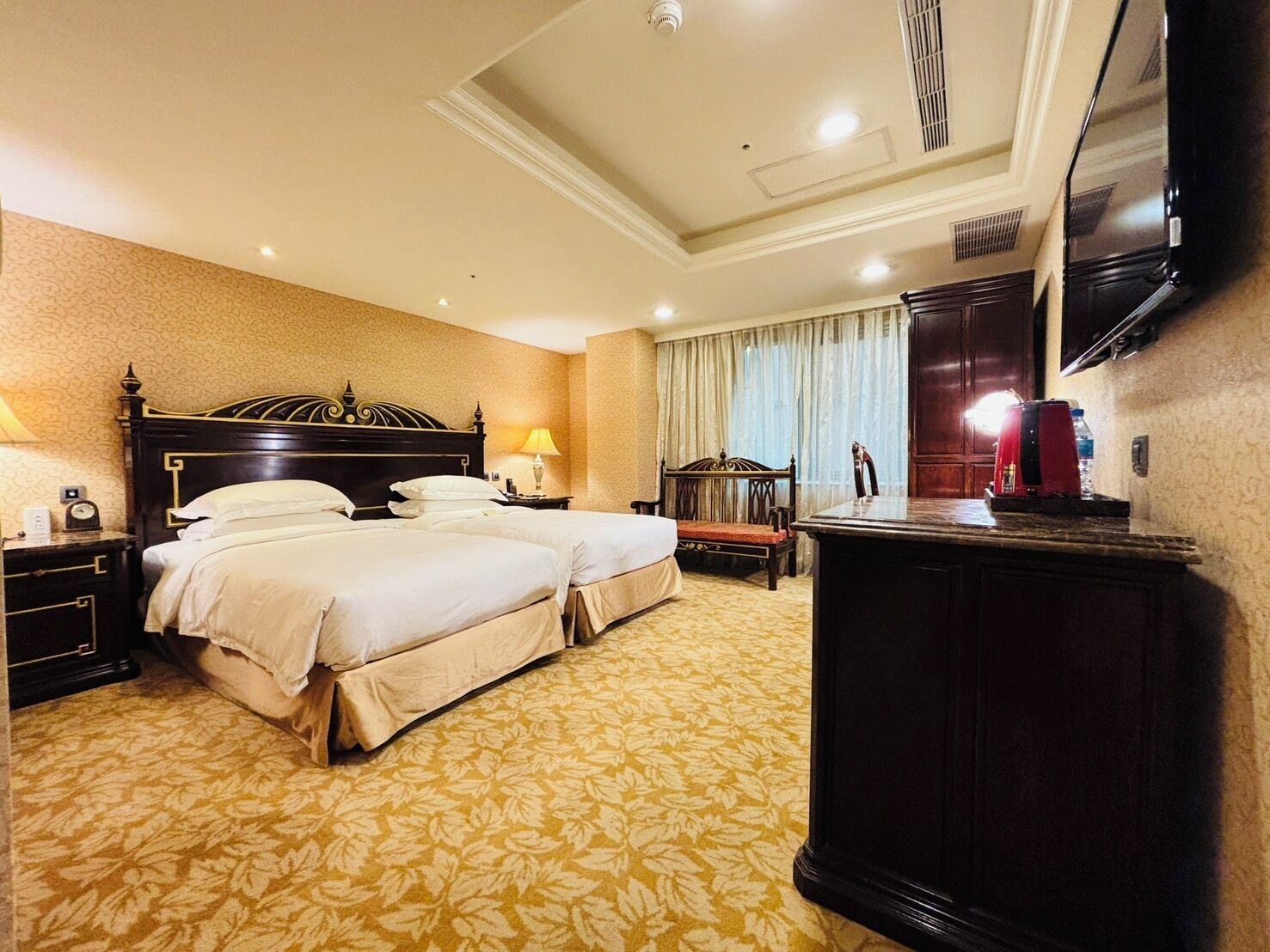 A hotel room with two beds, a desk, a chair, a television, and a minibar.