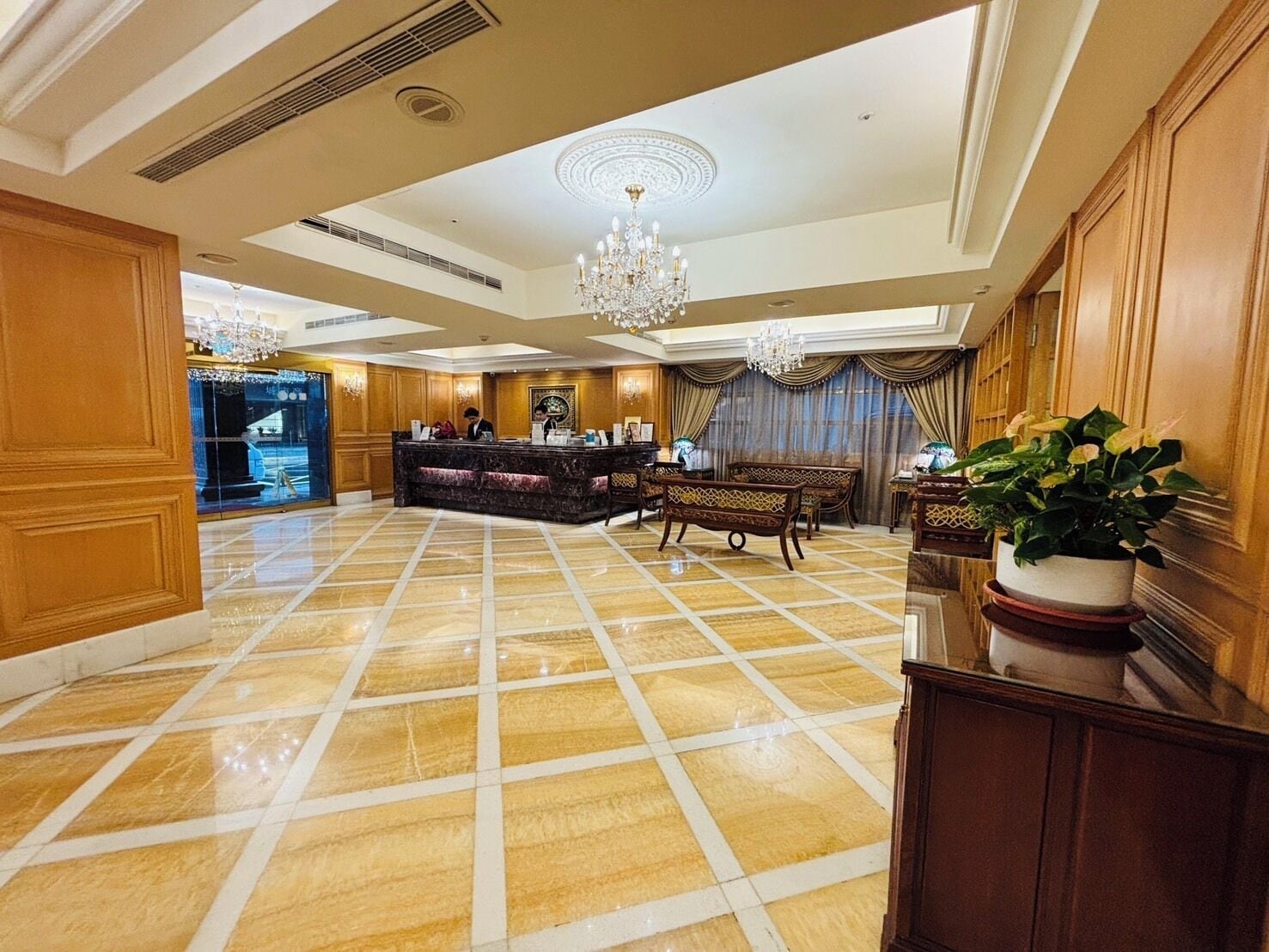 A spacious lobby with a marble floor, a reception desk, and a chandelier.