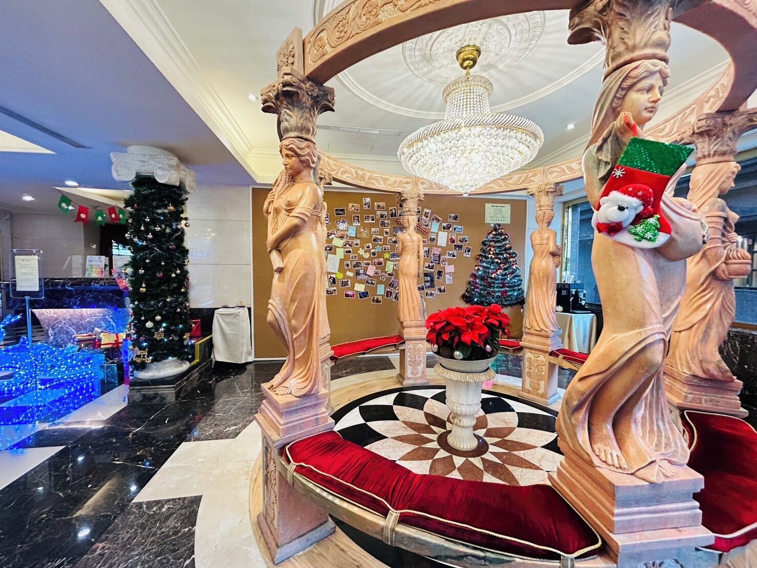 A luxurious lobby with marble flooring, a grand chandelier, and classical statues.