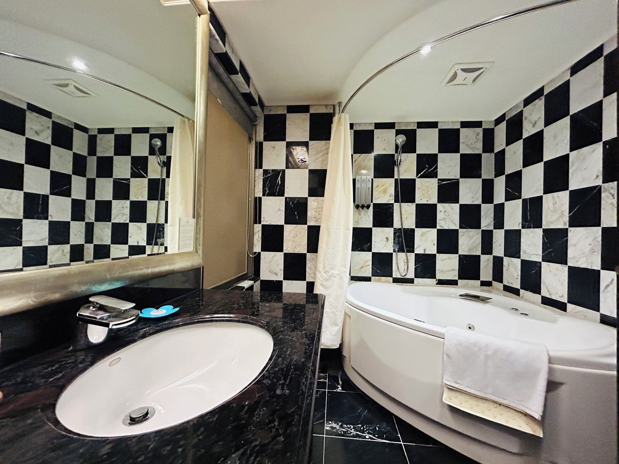 A bathroom with a checkered black and white tile wall, a white sink, and a bathtub with a towel.