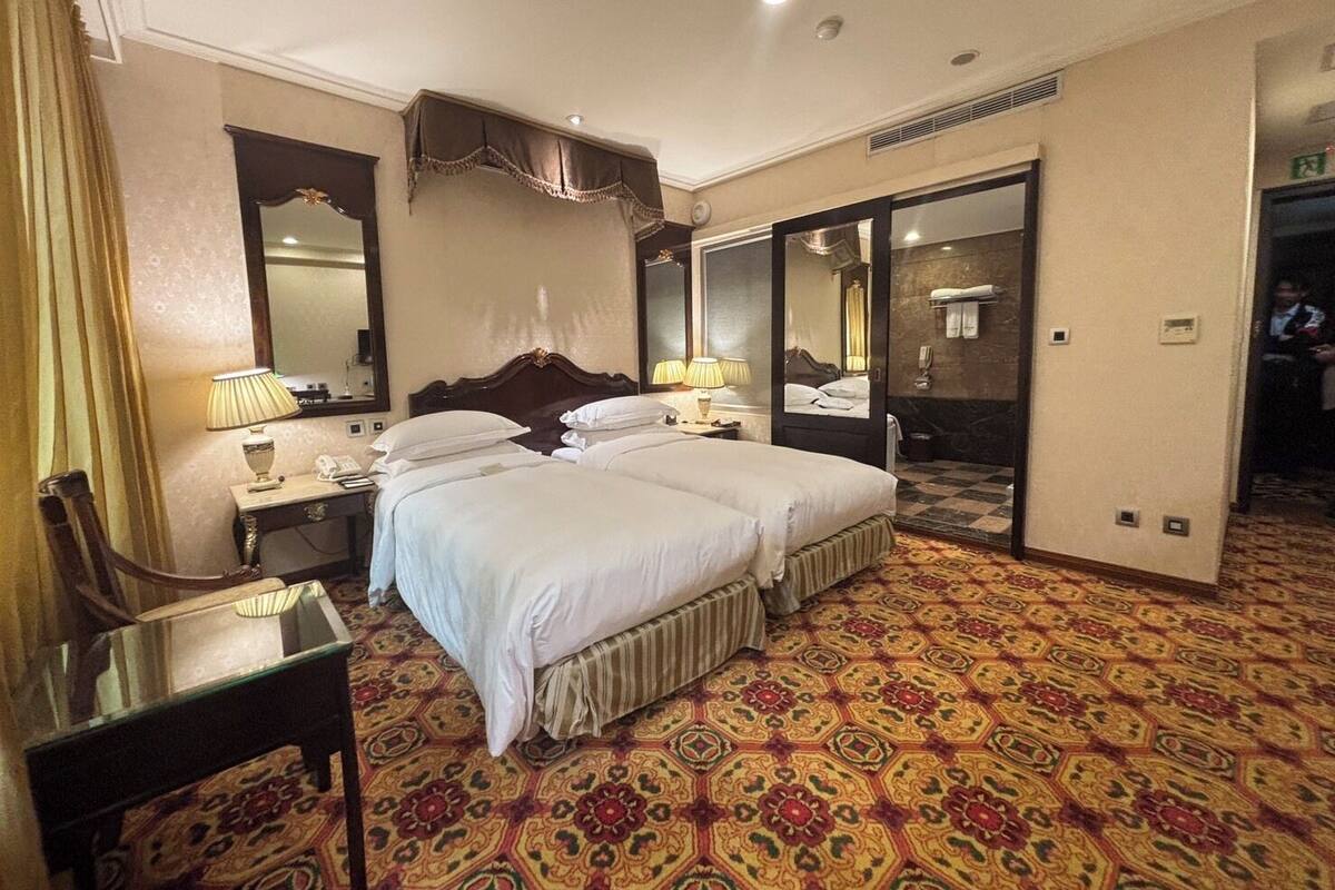 A hotel room with two beds, a desk, a chair, a mirror, and a bathroom visible through an open door.