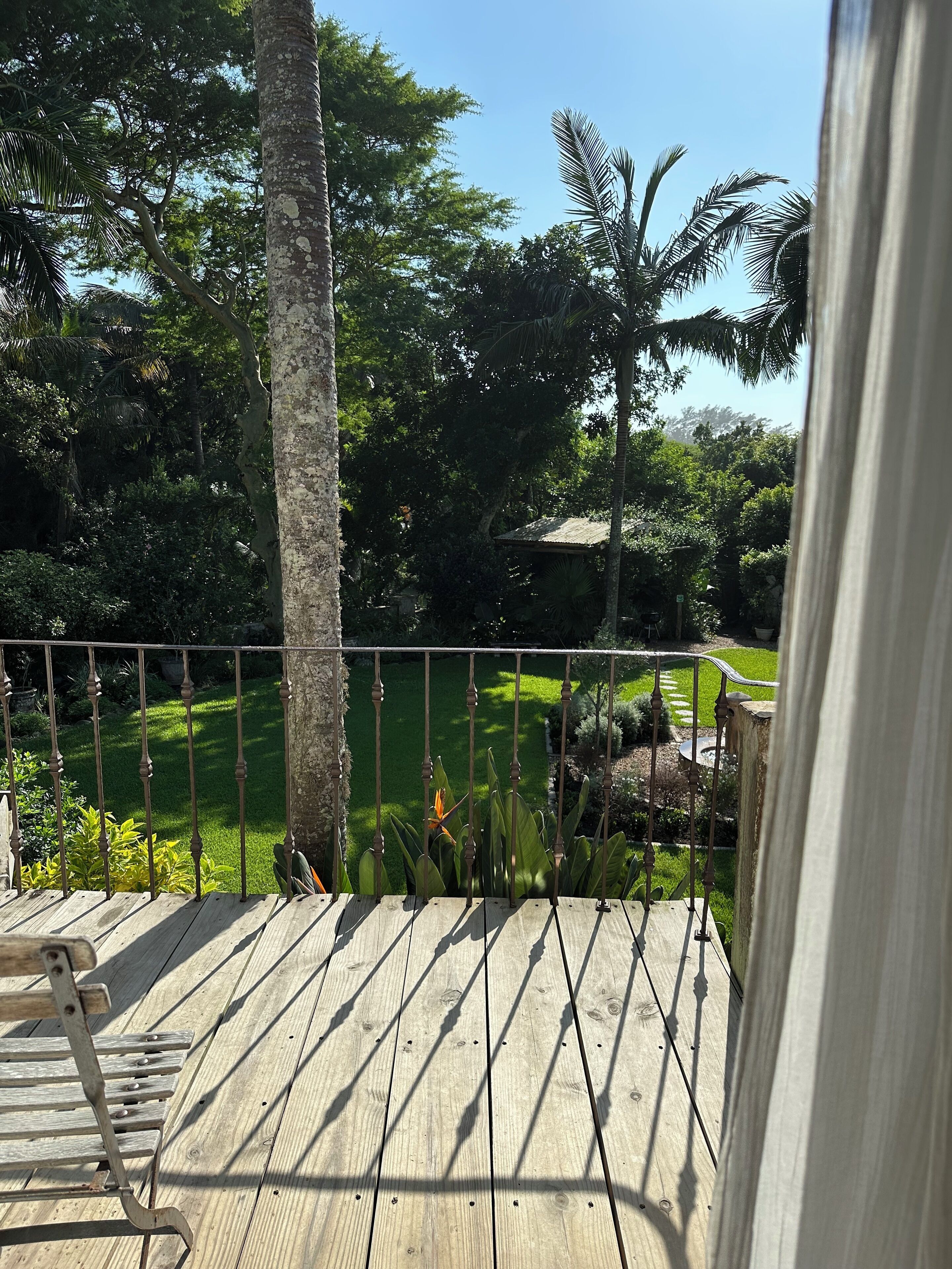 En træterrasse med gelænder i metal, med udsigt over en velplejet have med forskellige planter og træer.