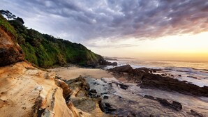 Eine Küstenlandschaft mit felsigem Ufer, einem Sandstrand und einem bewaldeten Felsen.