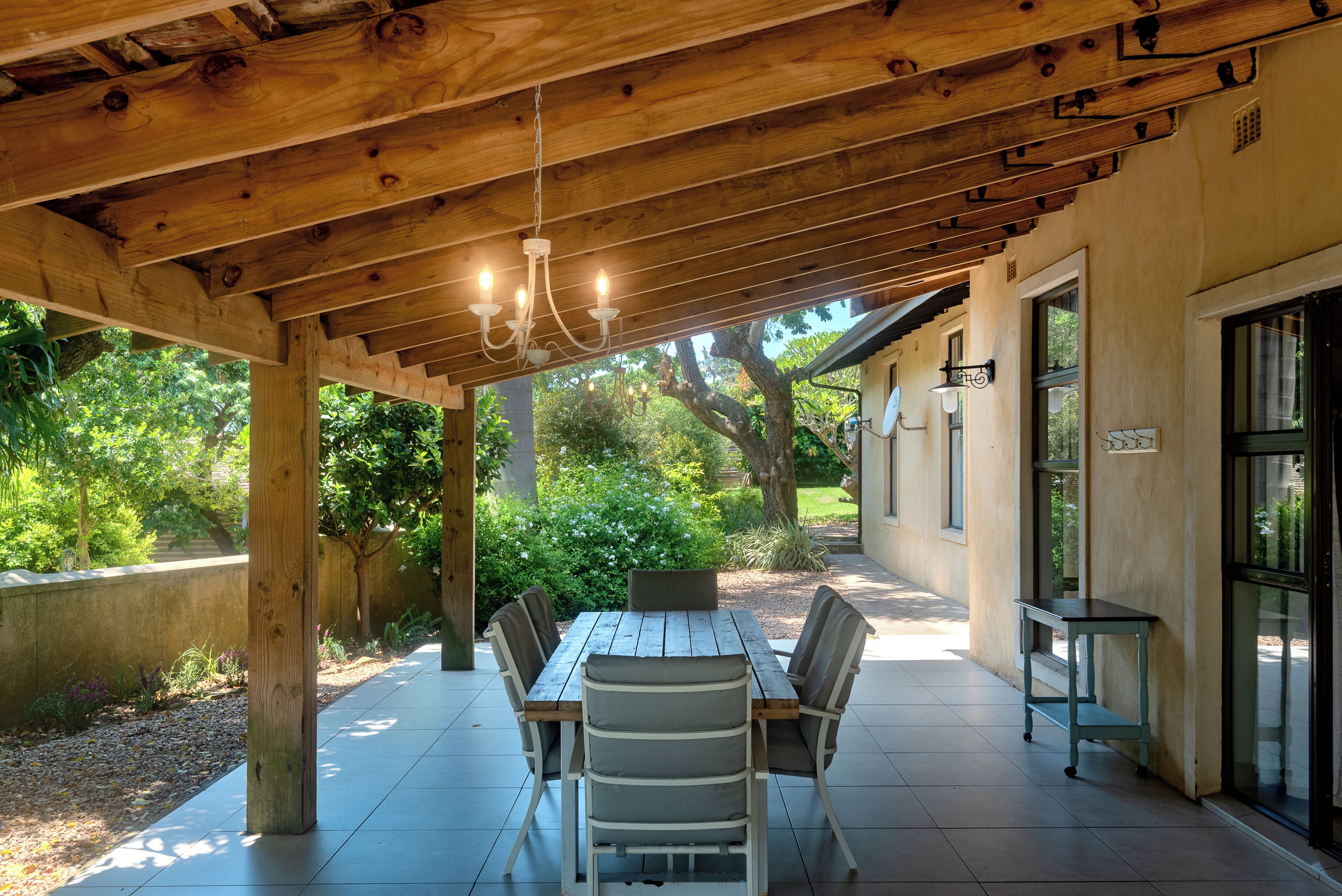 Een terras buiten met een houten pergola, een eettafel met stoelen en een kleine bijzettafel met een stoel.