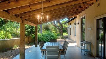 Een terras buiten met een houten pergola, een eettafel met stoelen en een kleine bijzettafel met een stoel.