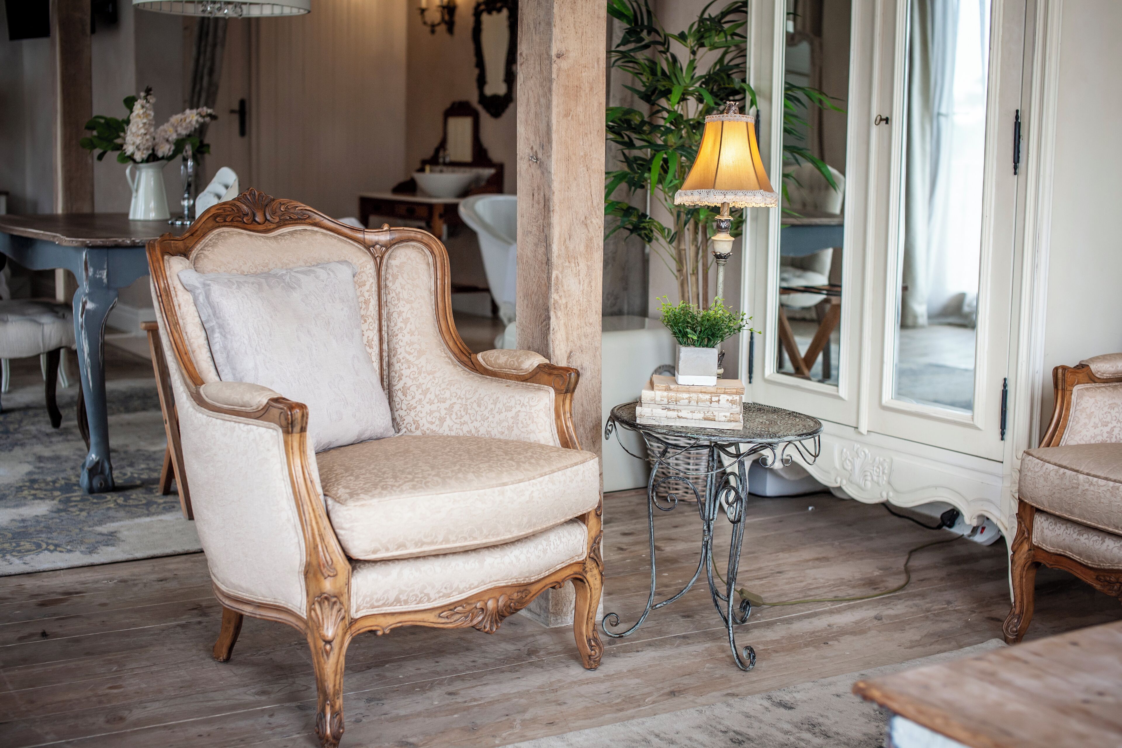 A classic room with a vintage armchair, a small table with a lamp, and a view of the outside through a glass door.