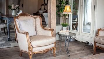A classic room with a vintage armchair, a small table with a lamp, and a view of the outside through a glass door.