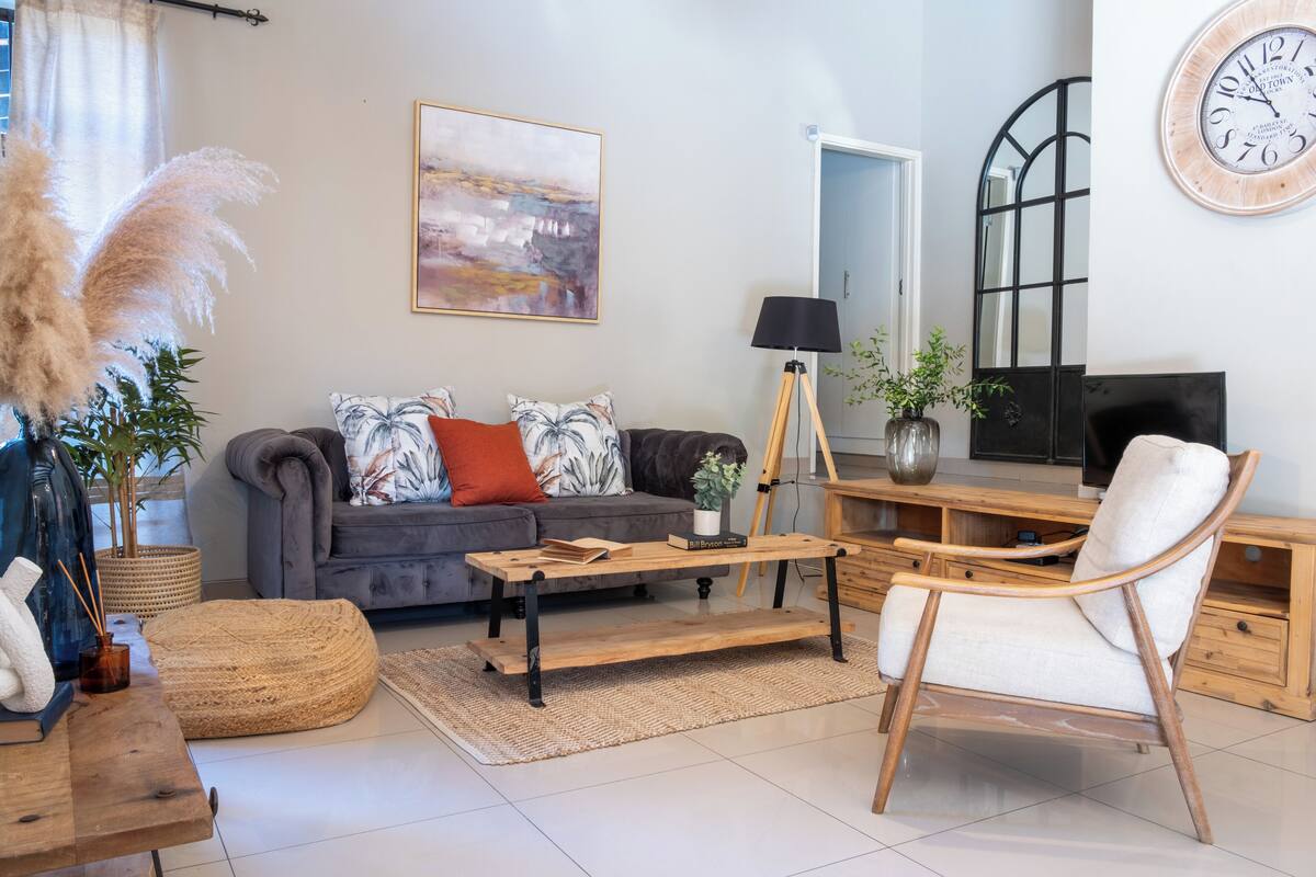 A living room with a grey sofa, a wooden coffee table, a white armchair, a large clock, and a painting on the wall.