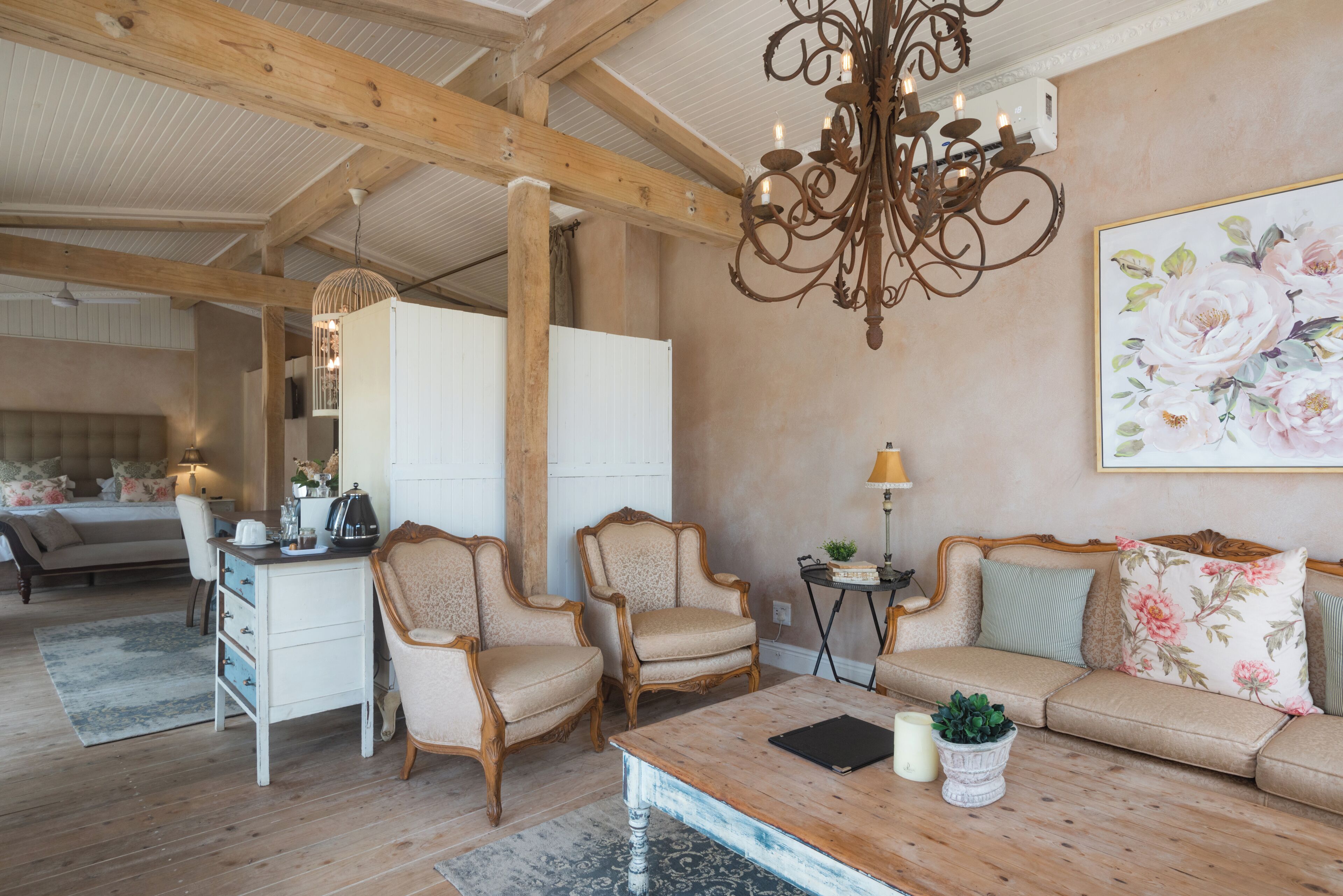 Una sala de estar acogedora con techo de madera, un candelabro, un sofá, dos sillones, una mesa de centro y un cuadro en la pared.