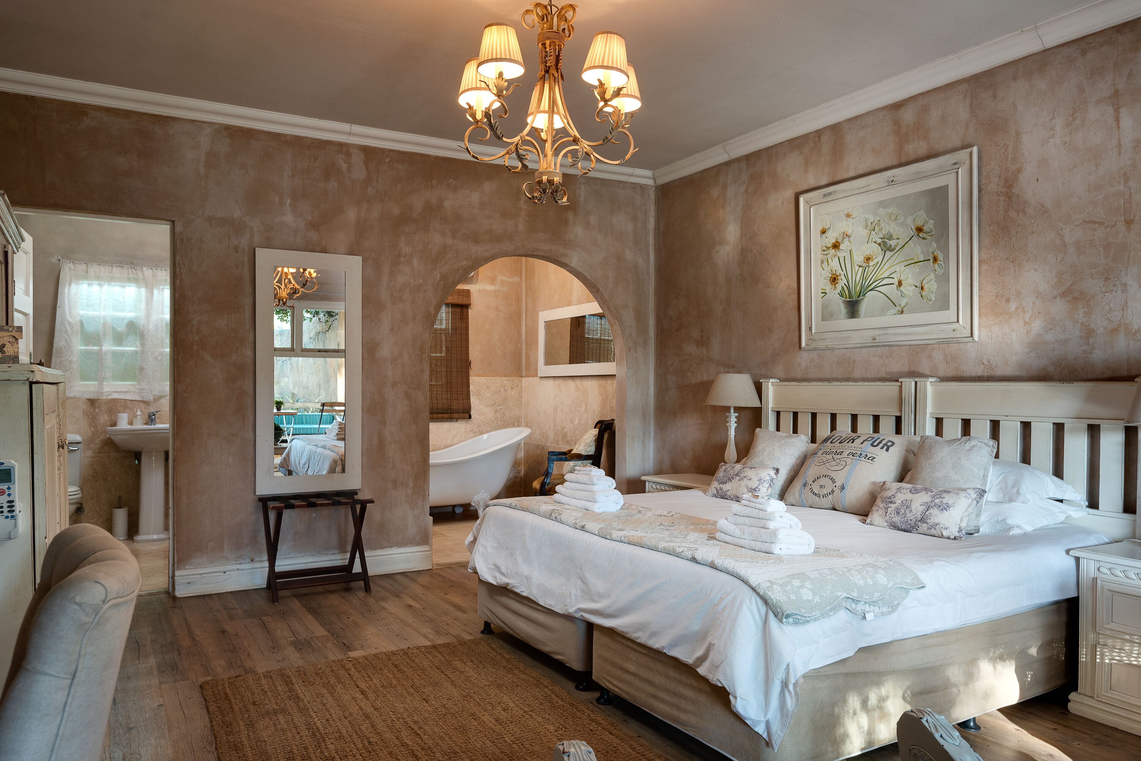 A bedroom with a large bed, a vanity, a bathtub, and a chandelier.