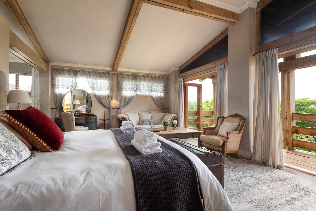 A spacious bedroom with a large bed, a desk, a chair, and a view of the outdoors.