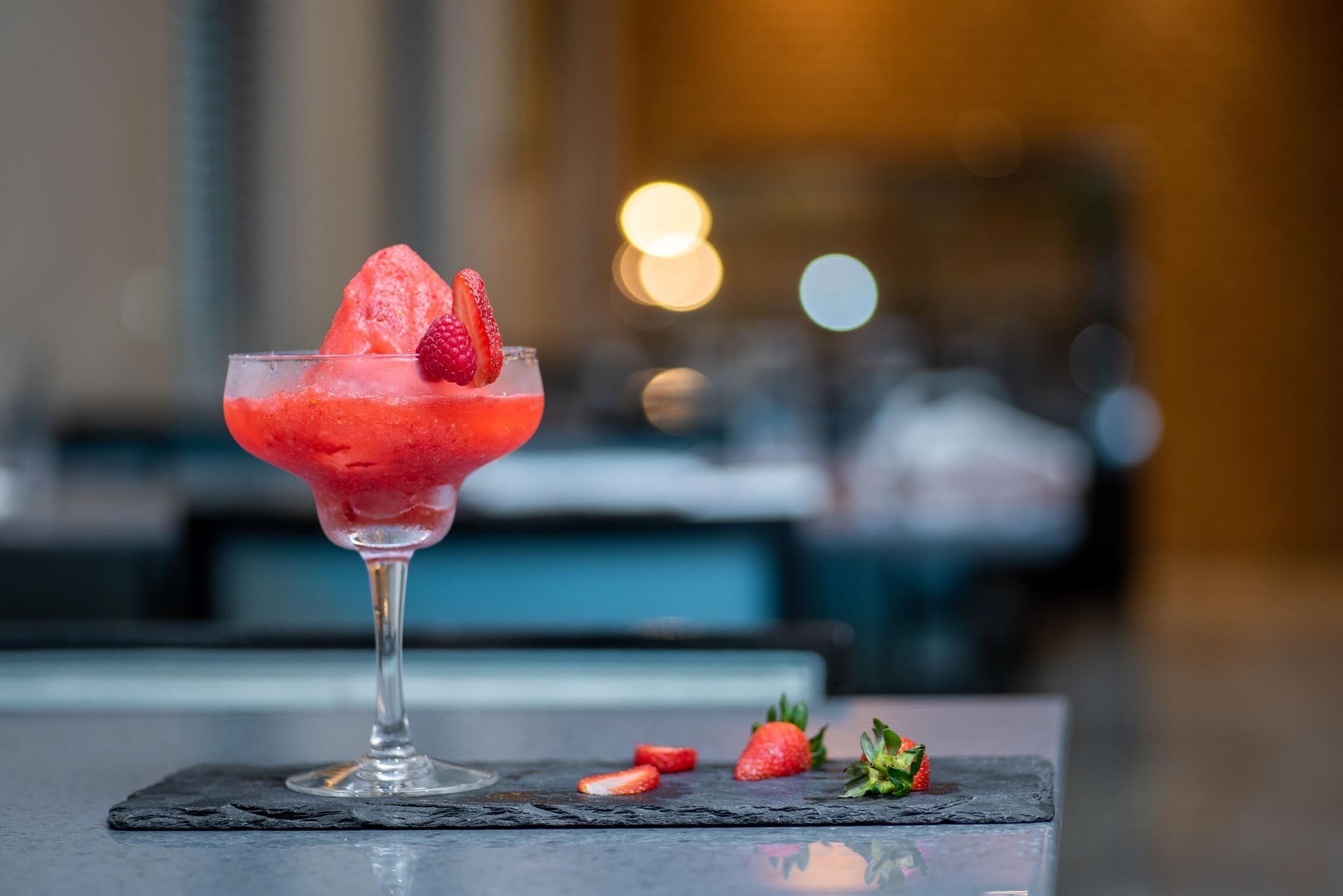 A cocktail glass with a strawberry garnish on a slate coaster.