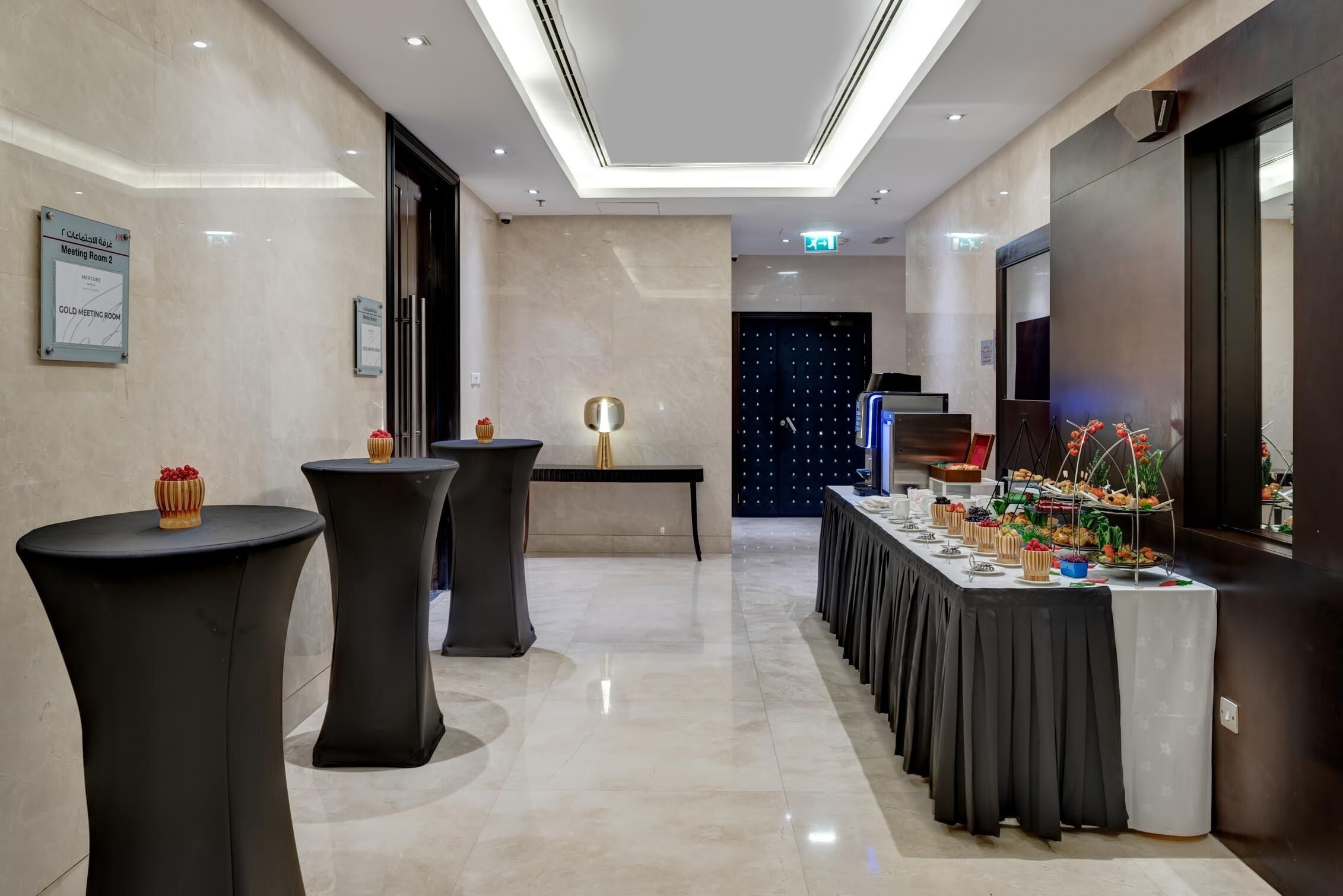 A modern hotel lobby with a long reception table, black round tables, and a meeting room sign.