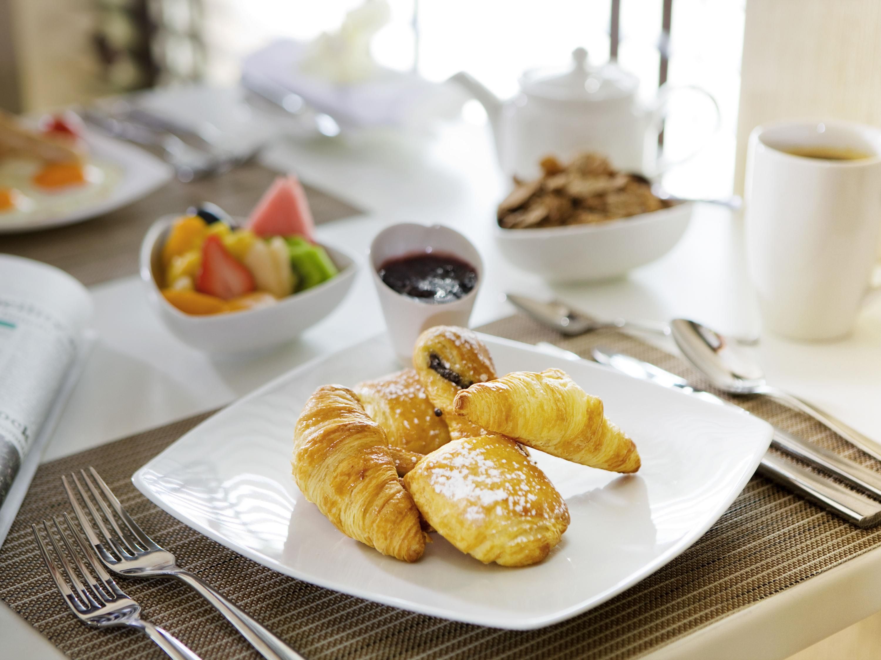 A breakfast setting with croissants, fruit, and a cup of coffee on a table.