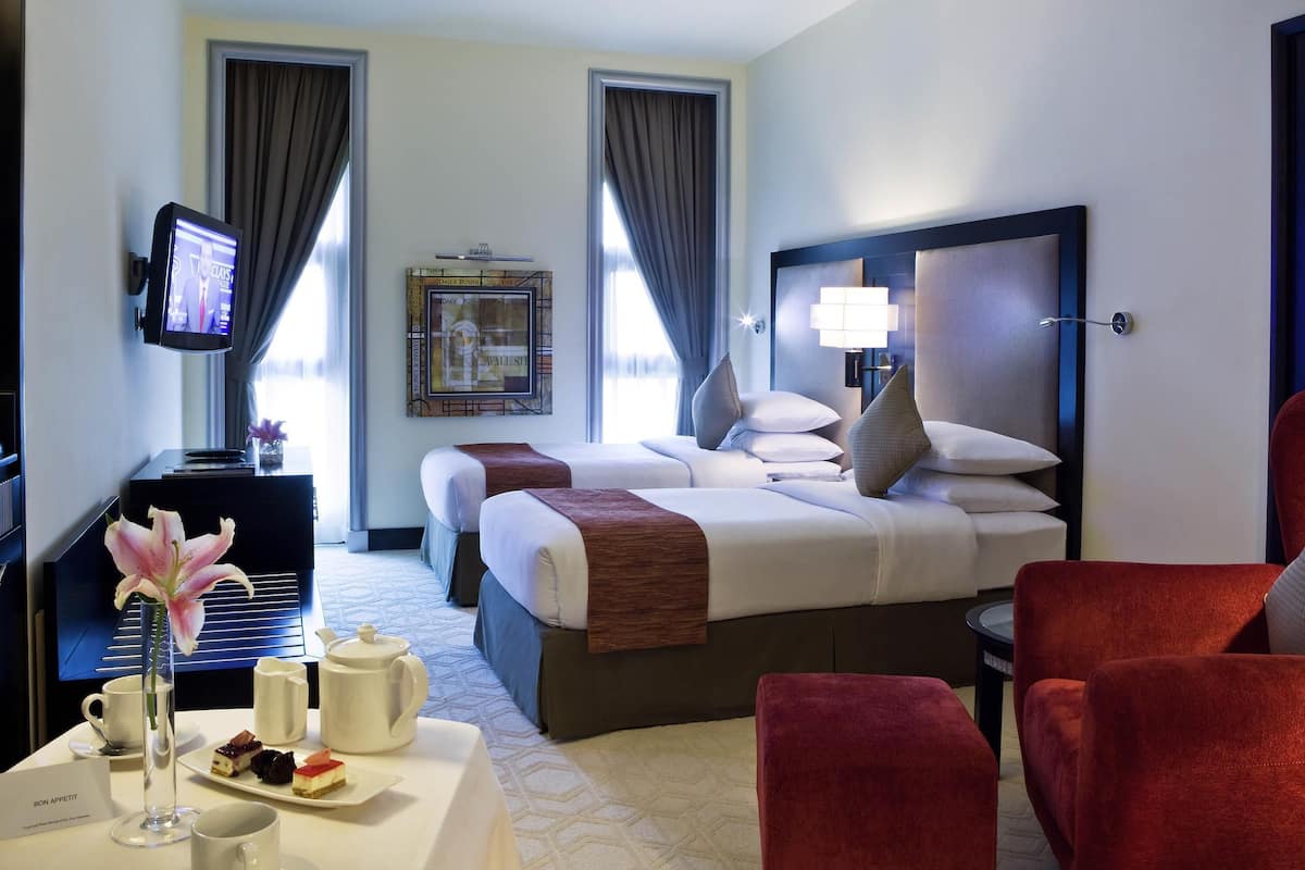 Ein Hotelzimmer mit einem Bett, Nachttischen, einem Fernseher, einer Lampe und einem roten Sessel.