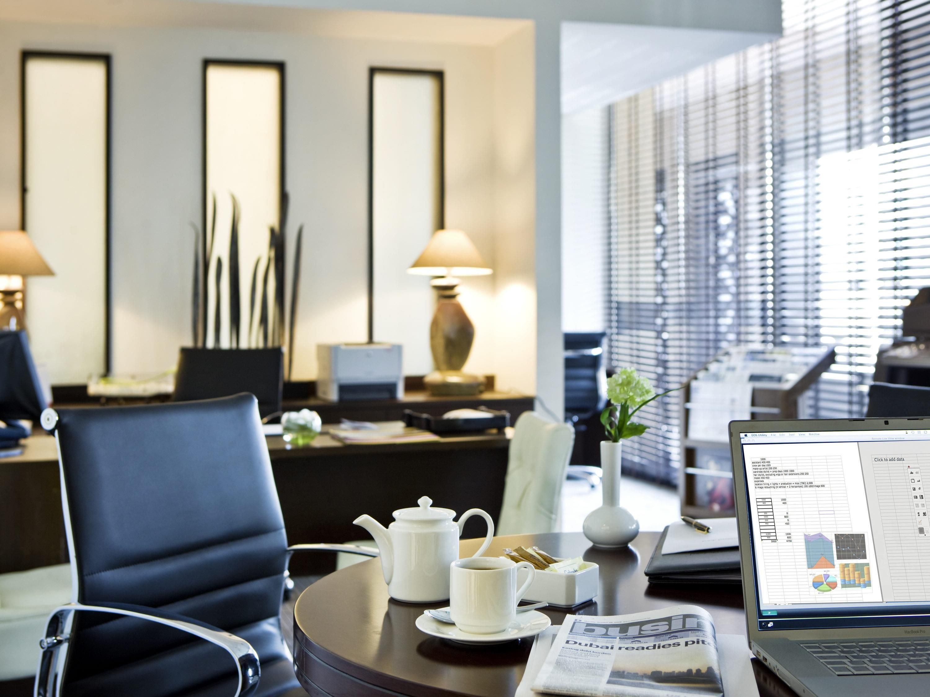 Une chambre d’hôtel moderne équipée d’un bureau, d’un ordinateur portable, d’une théière, d’une tasse et d’un journal.
