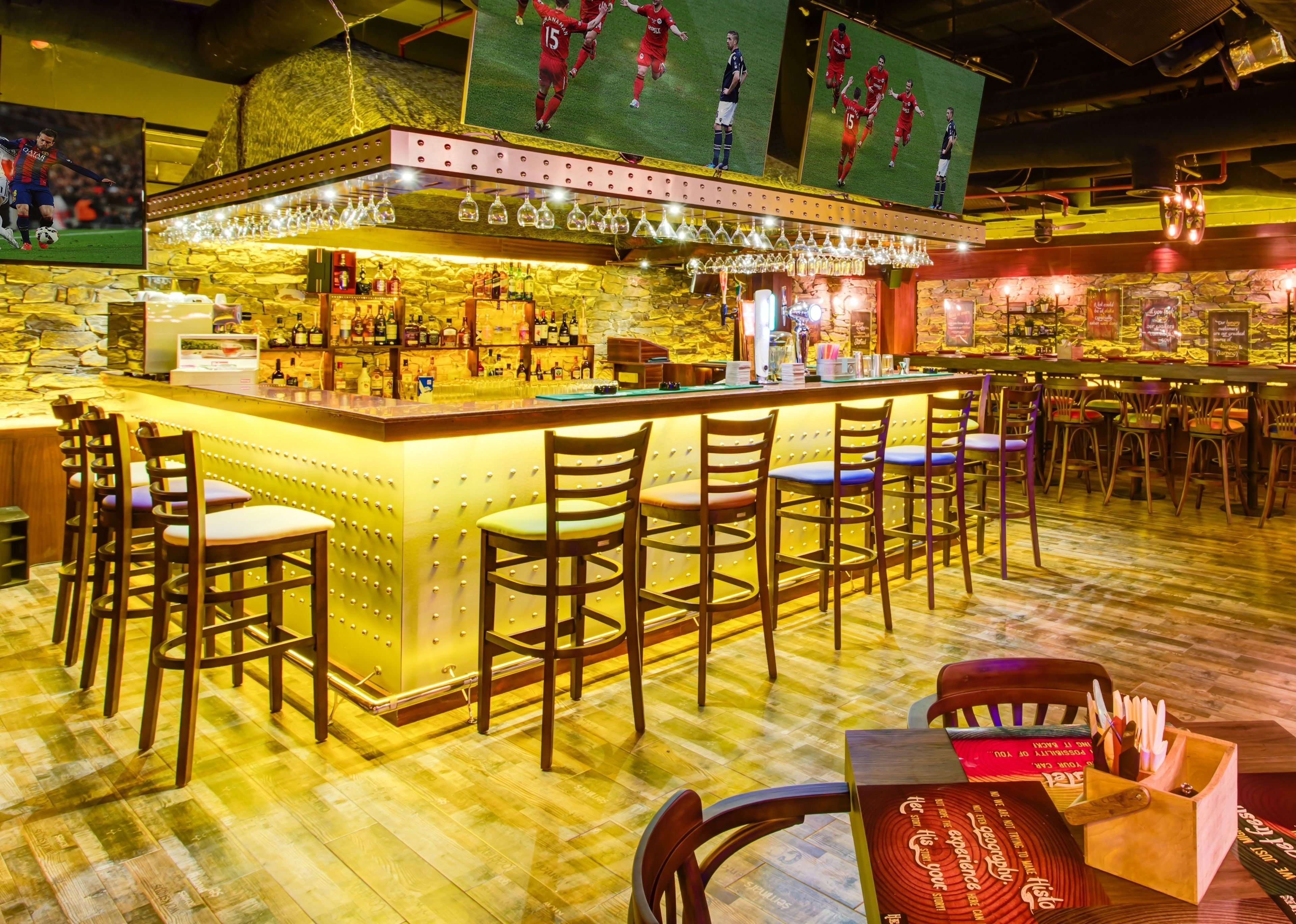 Zona de bar con mostrador, taburetes y una pantalla grande mostrando deportes.