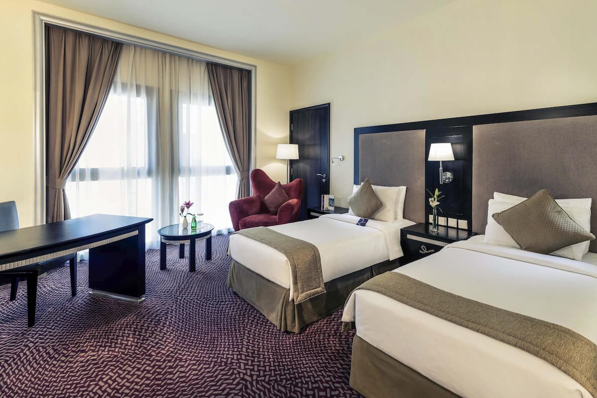 Ein Hotelzimmer mit zwei Betten, einem Schreibtisch, einem Stuhl, einem kleinen Tisch und einer Lampe.