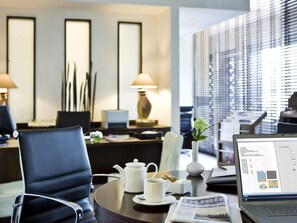 A modern hotel room with a desk, laptop, teapot, cup, and newspaper.