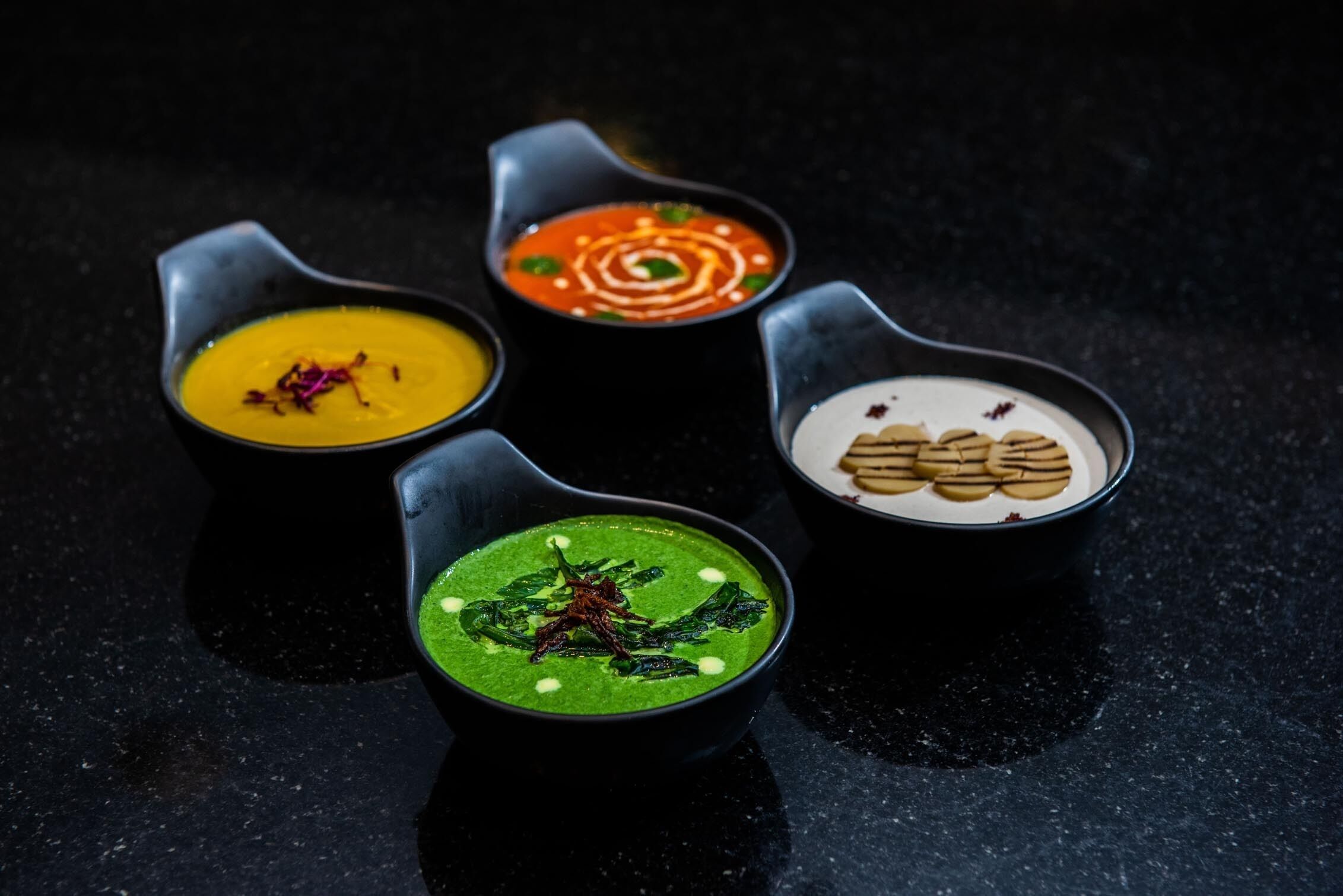 Four bowls of soup on a dark surface.