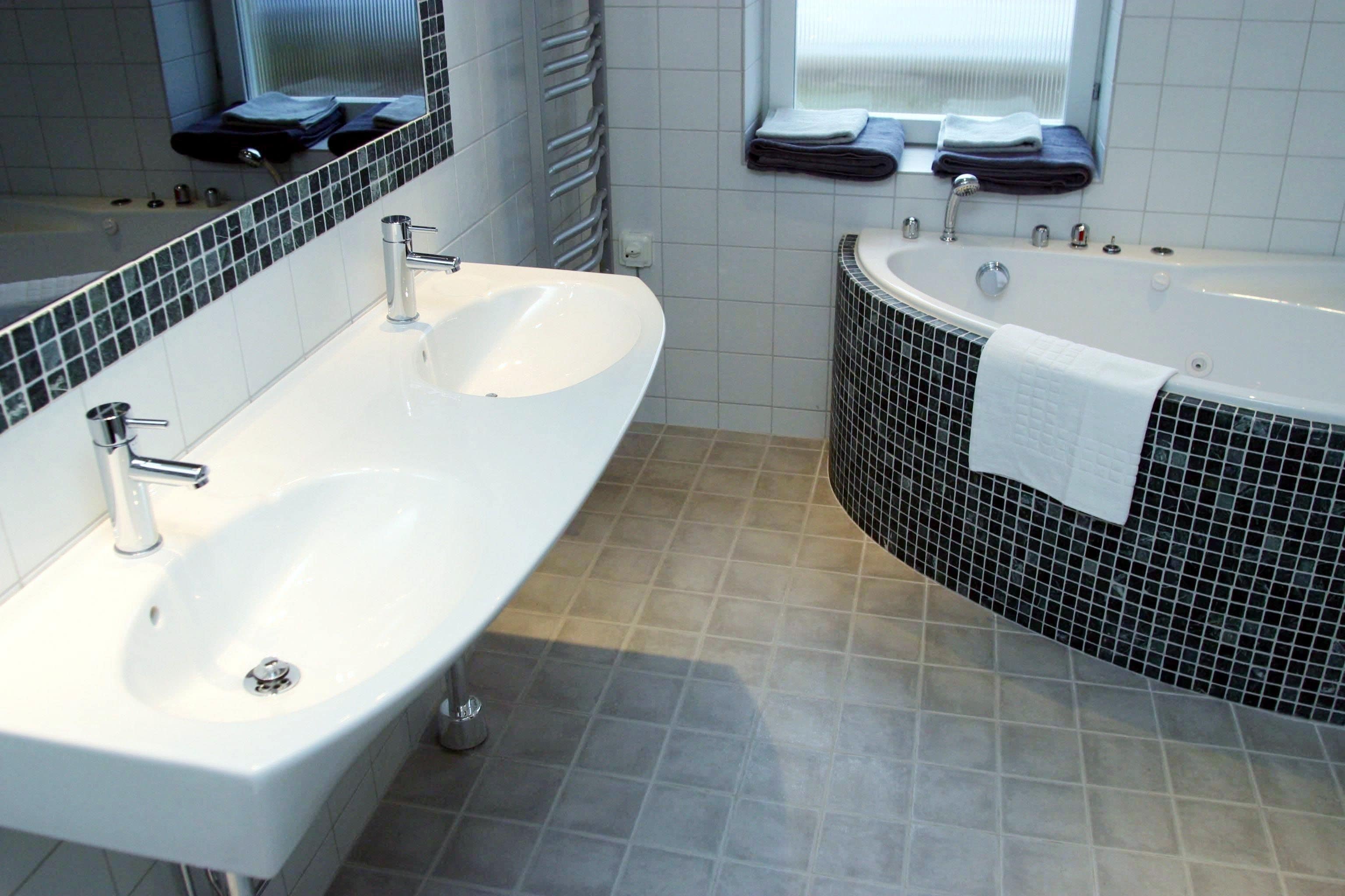 Un baño moderno con dos lavamanos, una bañera y una ventana con toallas.