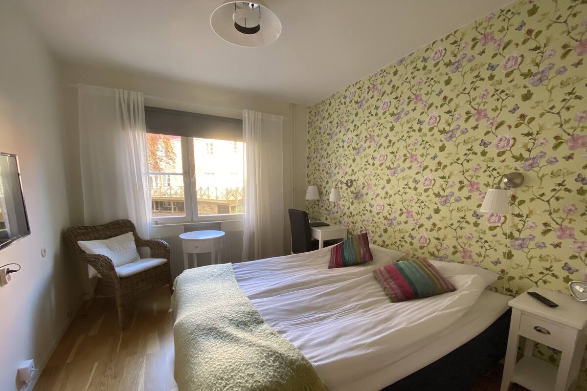 A bedroom with a bed, a chair, a small table, and a window with curtains.